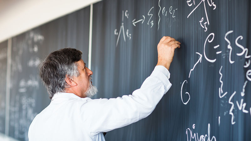 Aurora Analytics Home, Chemistry Education: Background image of a professor solving an equation written on a chalkboard